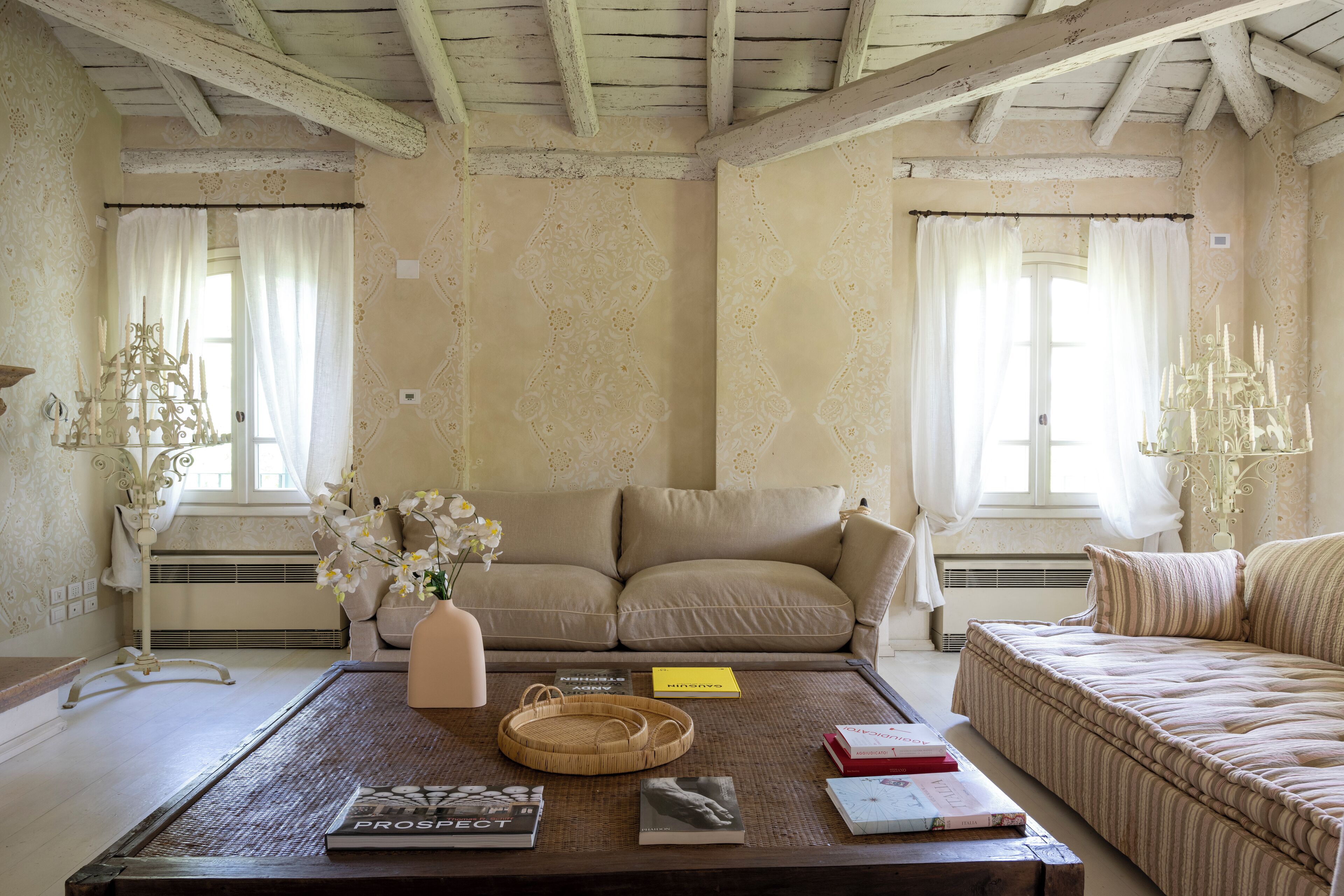 Una sala de estar acogedora con un sofá color beige, una mesa de centro con libros y un jarrón de flores, y un papel tapiz estampado.