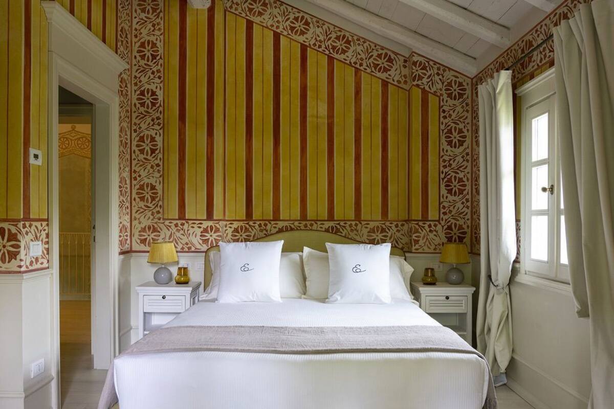 A hotel room with a large bed, two bedside tables with lamps, a patterned wall, and a window with curtains.