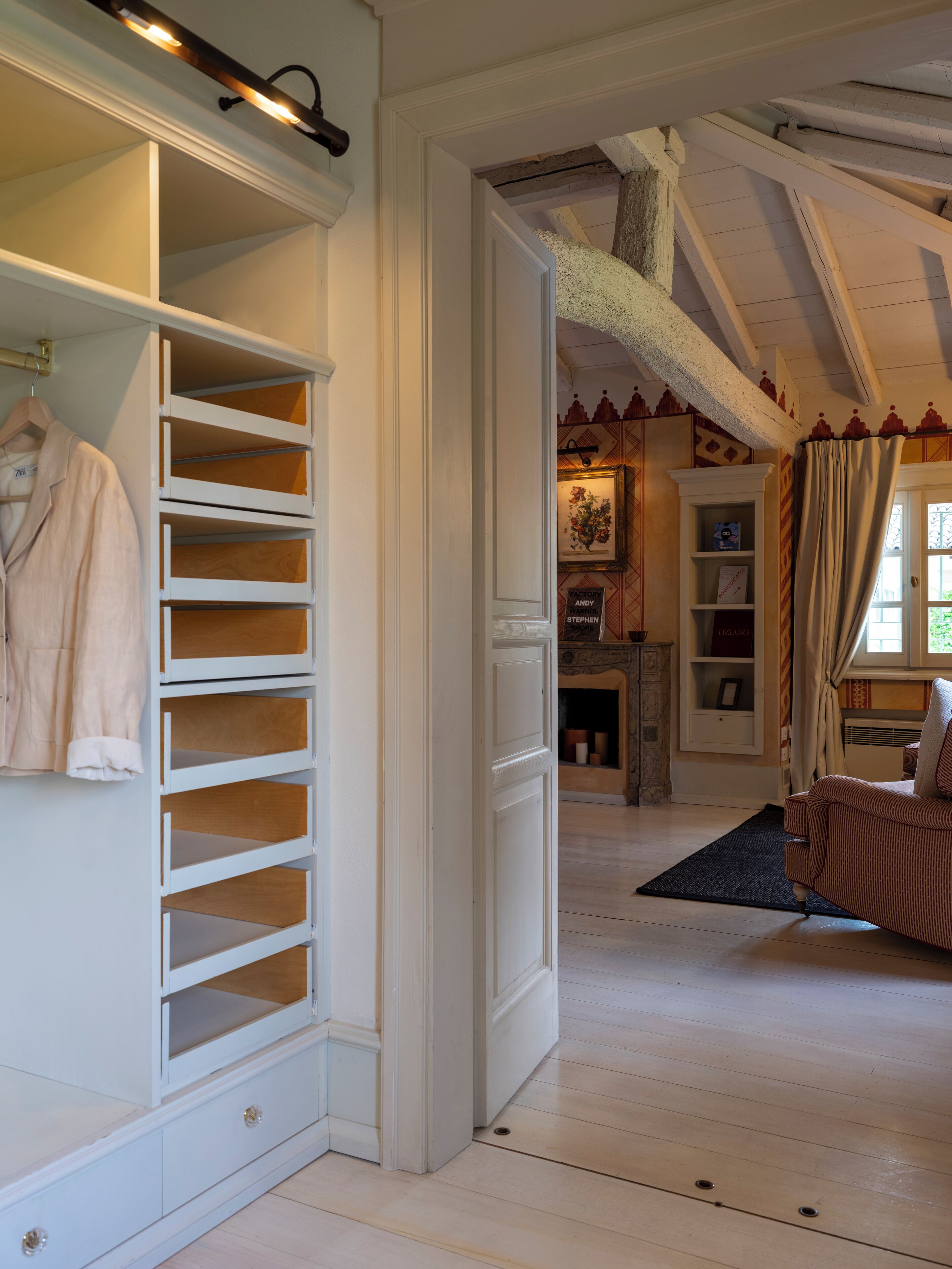 Habitación con armario empotrado blanco, suelo de madera, techo estampado y una zona de estar acogedora con sofá estampado.