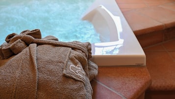 A hot tub with a towel on the edge, a window with a plant, and a tiled floor.