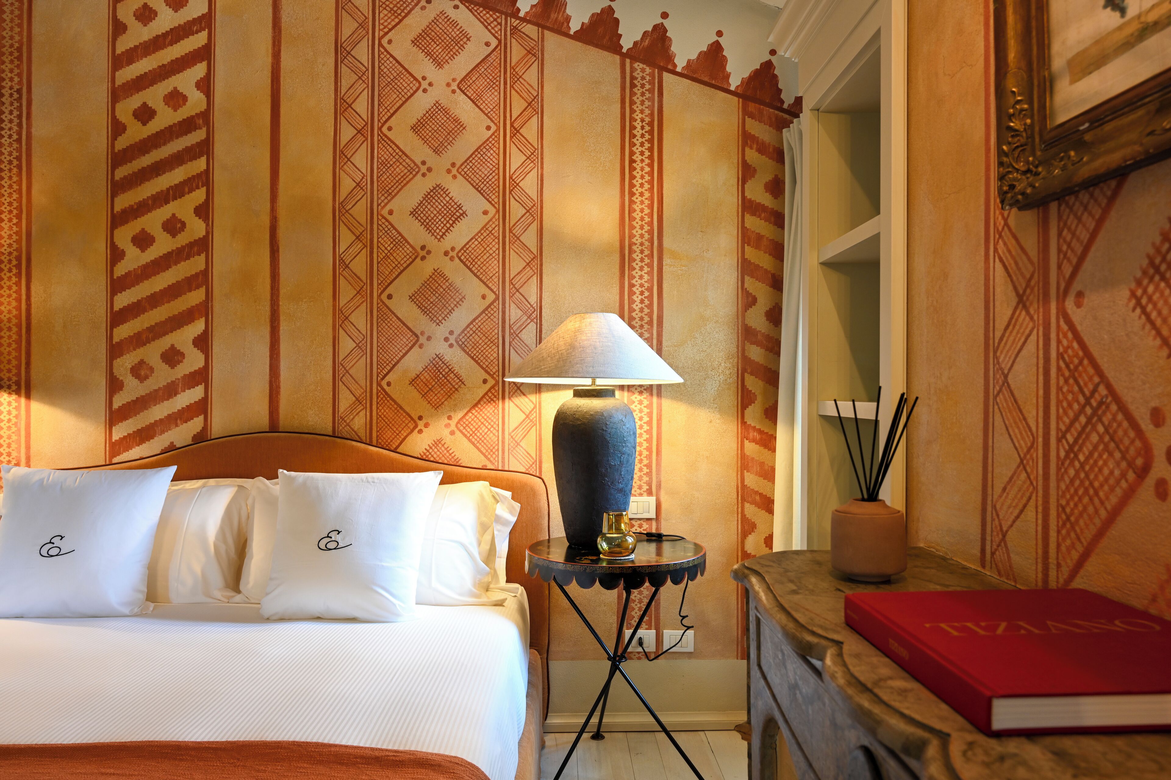 Una habitación de hotel con cama, lámpara, un libro y decoración en la pared.