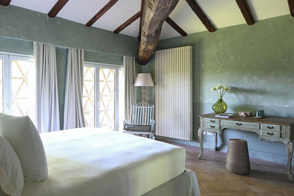 A bedroom with a bed, a desk, a chair, a lamp, and a window with curtains.