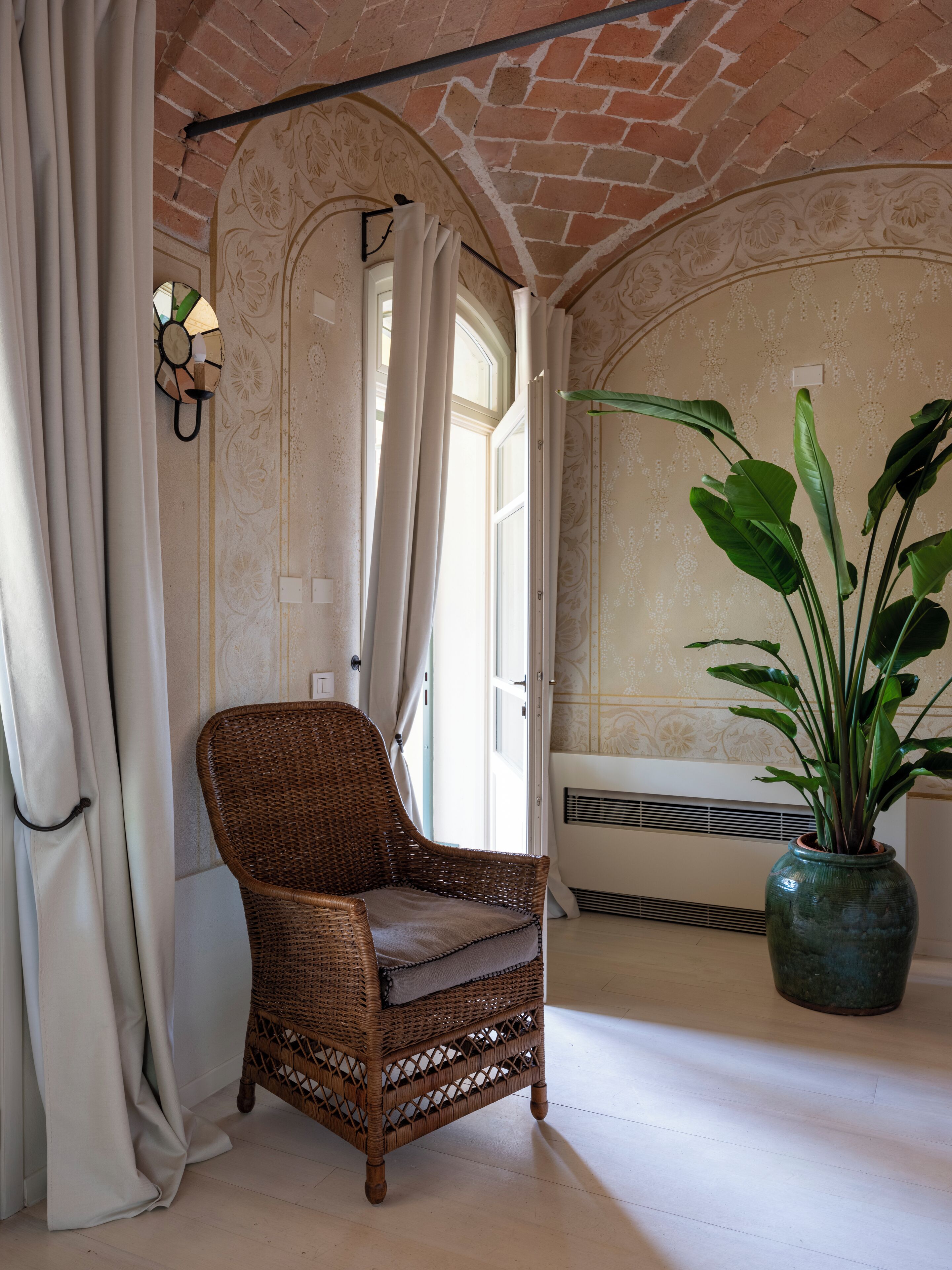 Une chaise en osier avec un coussin, une plante en pot et une fenêtre avec des rideaux.