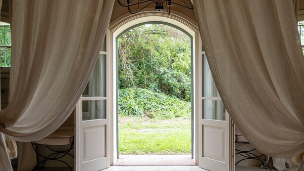 Una camera da letto con un grande letto, una testata in legno e vista attraverso una finestra con tende.