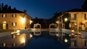 Una piscina con un riflesso limpido, circondata da due grandi edifici con molte finestre e un'area relax coperta.