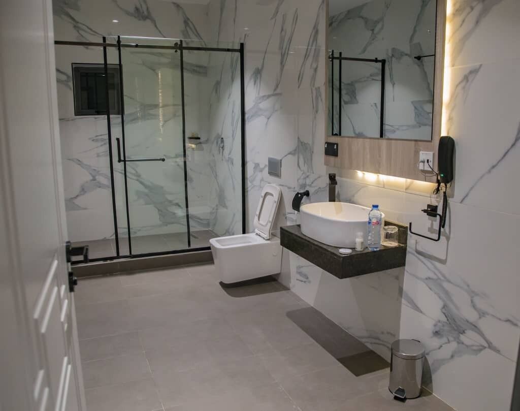 A modern bathroom with a glass-enclosed shower, a white toilet, and a marble-tiled vanity with a sink and mirror.