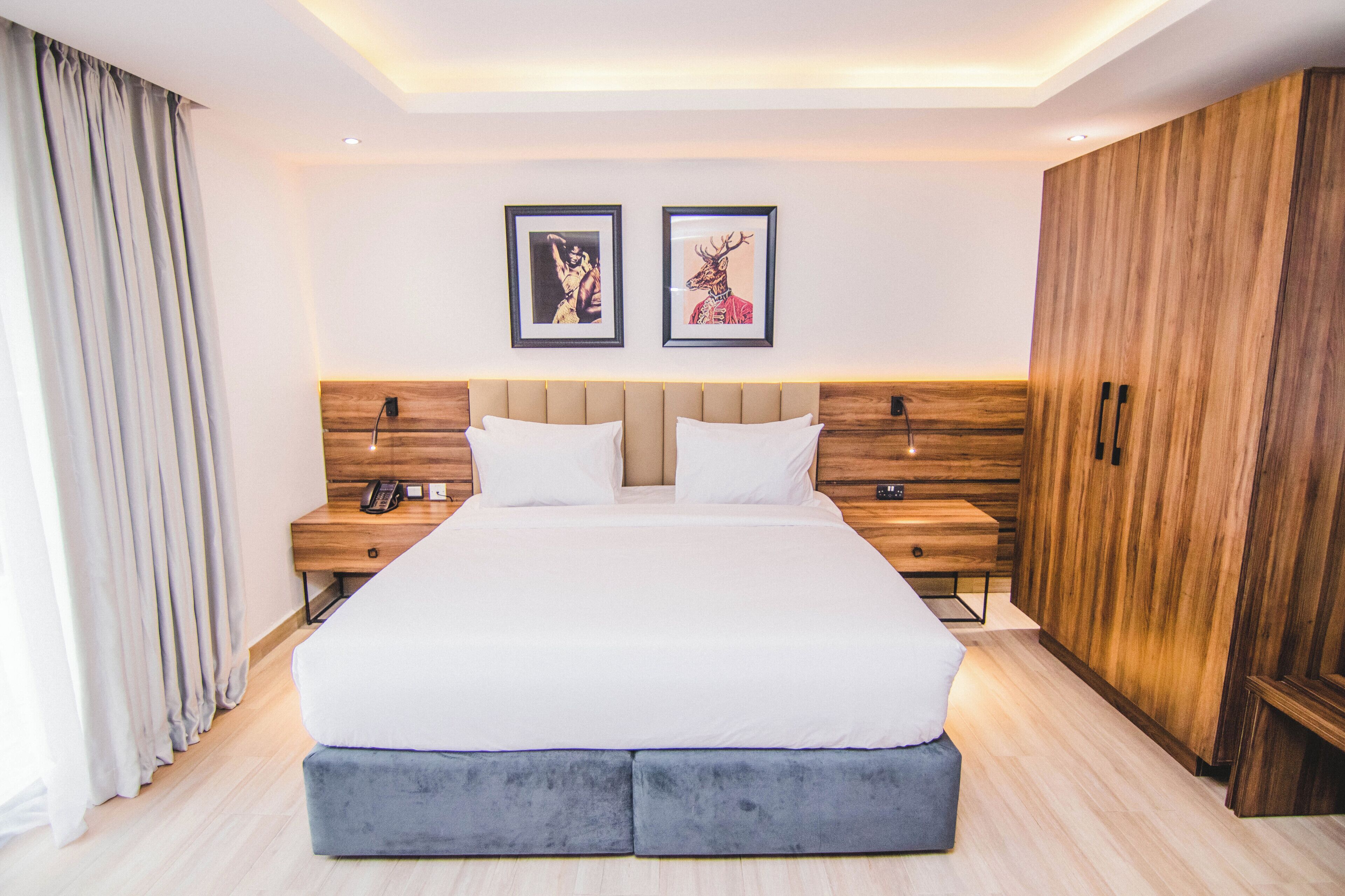 A modern hotel room with a large bed, wooden headboard, two bedside tables with lamps, and a wardrobe.