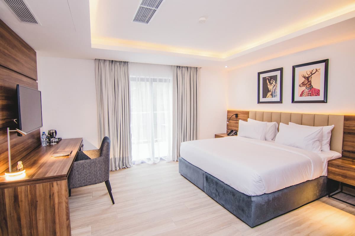 Une chambre d’hôtel moderne, dotée d’un grand lit, d’un bureau avec une chaise, d’un téléviseur à écran plat et de deux tableaux encadrés au mur.