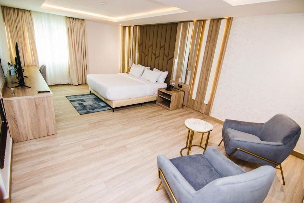 A modern hotel room with a large bed, a desk, a chair, and a small table.