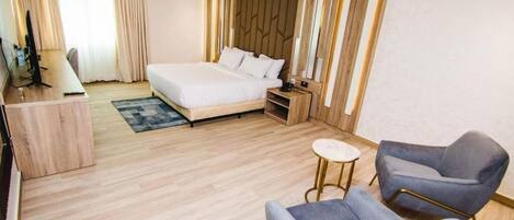 A modern hotel room with a large bed, a desk, a chair, and a small table.