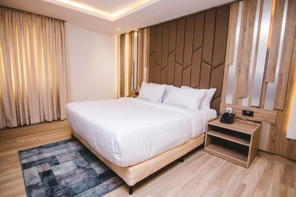 Ein modernes Hotelzimmer mit einem großen Bett, einem Holzkopfteil und einem Nachttisch mit Telefon.