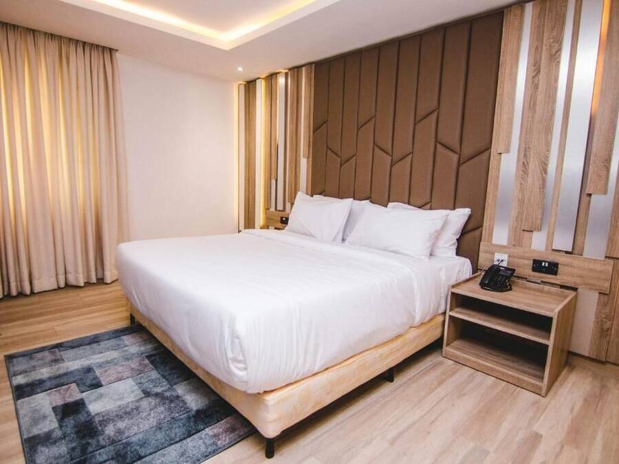 Quarto de hotel moderno com cama grande, cabeceira de madeira e mesa de cabeceira com telefone.