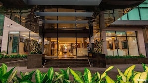 A modern hotel entrance with a glass facade, outdoor seating area, and a staircase leading to the lobby.