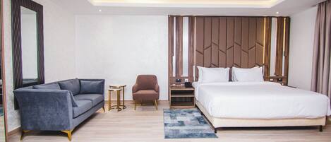 Une chambre d’hôtel moderne avec un grand lit, un canapé, un fauteuil et une petite table.