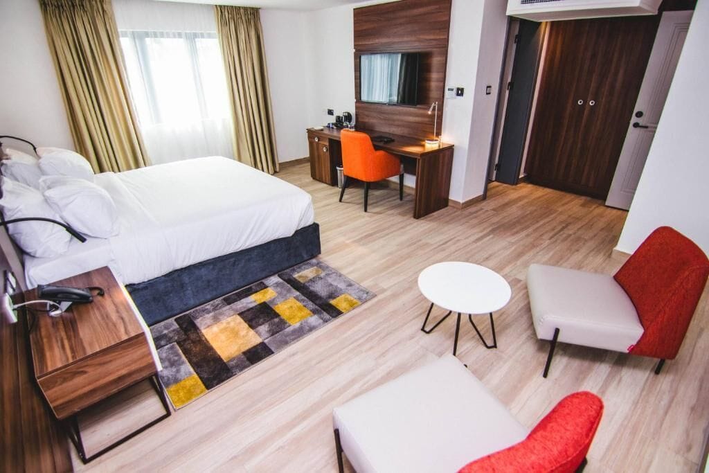 A hotel room with a bed, desk, two chairs, a small table, and a wardrobe.