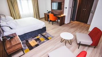 A hotel room with a bed, desk, two chairs, a small table, and a wardrobe.
