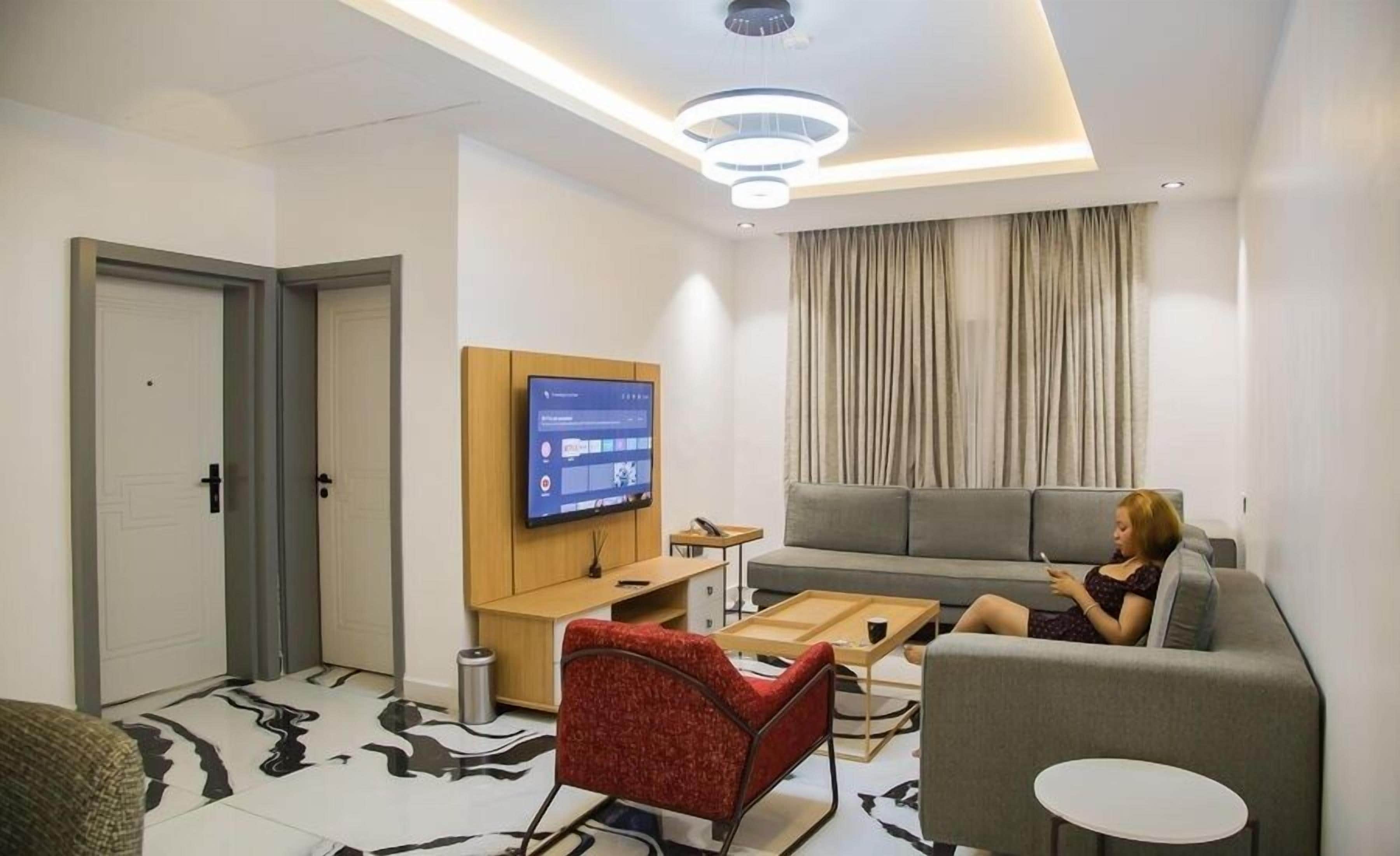 A modern living room with a flat-screen TV, a grey sofa, a red armchair, and a small round table.