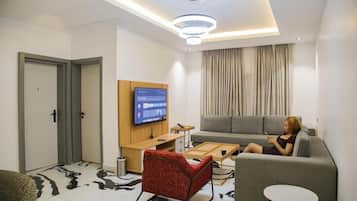 Una sala de estar moderna con un televisor de pantalla plana, un sofá gris, un sillón rojo y una pequeña mesa redonda.