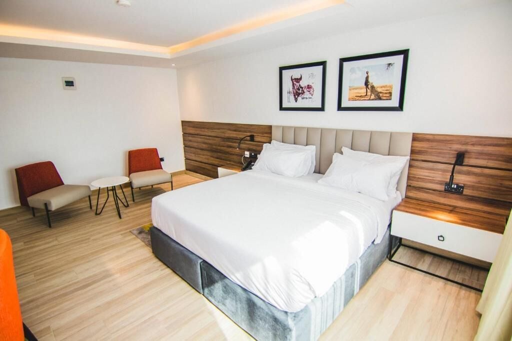 Una habitación de hotel moderna con una cama grande, una mesita de noche, una silla y dos cuadros en la pared.