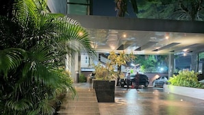 A well-lit outdoor area with a paved walkway, potted plants, and parked cars.