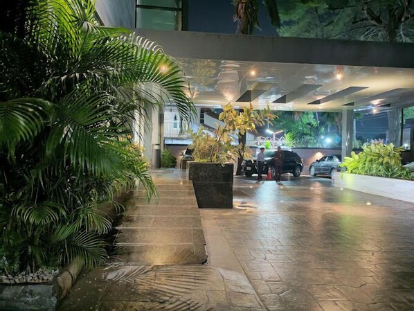 A well-lit outdoor area with a paved walkway, potted plants, and parked cars. - The Safron Hotel Ikeja (Lagos)