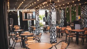 An indoor dining area with round tables and chairs, a TV mounted on the wall, and decorative string lights.