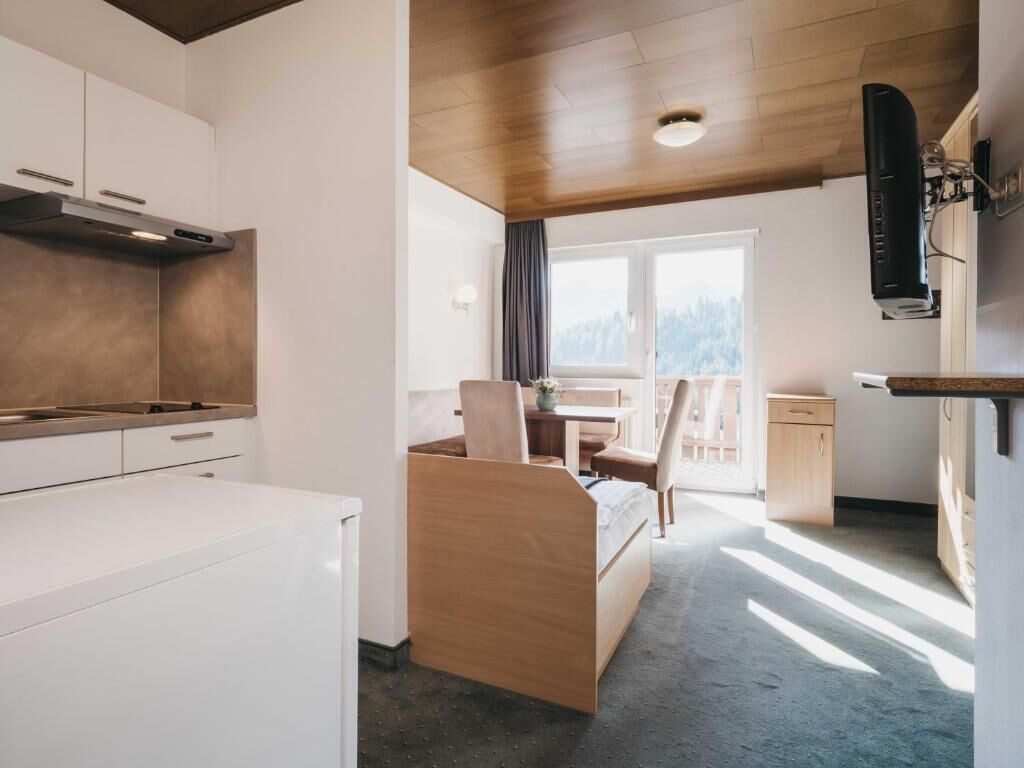Ein kleines Zimmer mit Küchenzeile, einem Bett, einem Schreibtisch und einem Fenster mit Blick ins Freie.