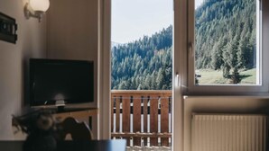 Una habitación con televisión, terraza de madera y vista a una montaña boscosa.