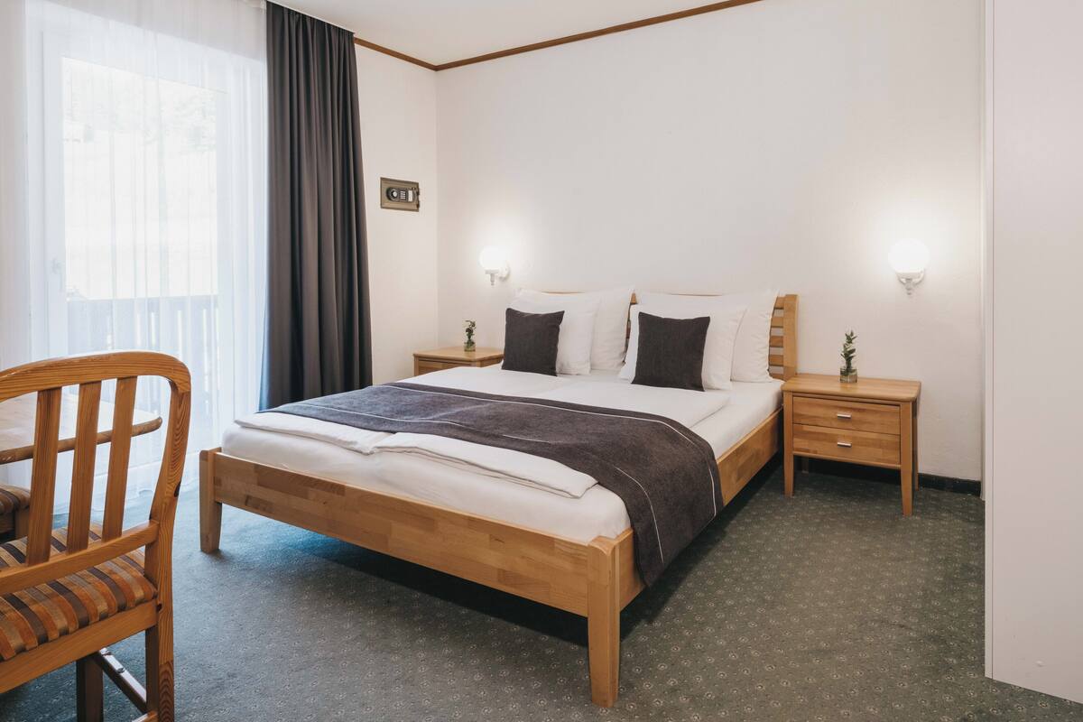 A hotel room with a wooden bed, two bedside tables, a chair, and a window with curtains.
