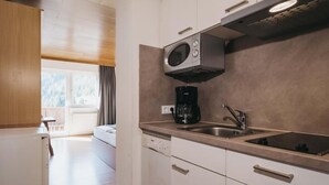 Una cocina moderna con armarios blancos, microondas integrado, cafetera y lavamanos.