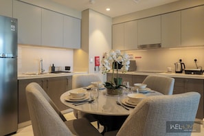 A modern kitchen with a dining area, featuring a round table with chairs, a refrigerator, and a coffee maker.