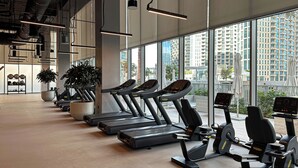 A modern gym with treadmills, stationary bikes, and a large window offering a city view. - WelHome - Exclusive 2BR Apartment in Downtown Forte (Dubai)