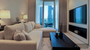 A modern hotel room with a large sofa, a flat-screen TV, and a balcony with a city view. - WelHome - Exclusive 2BR Apartment in Downtown Forte (Dubai)