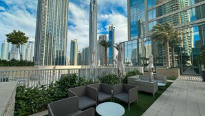 A rooftop terrace with outdoor seating, palm trees, and a city skyline in the background. - WelHome - Exclusive 2BR Apartment in Downtown Forte (Dubai)