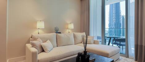 A modern living room with a beige sofa, two lamps, a coffee table, and a view of a cityscape through large windows.