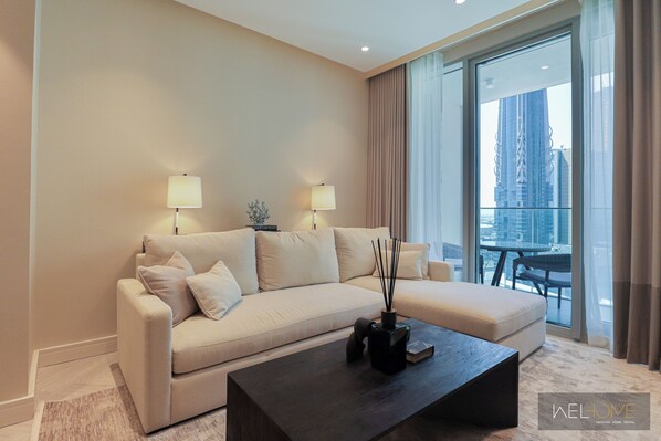A modern living room with a beige sofa, two lamps, a coffee table, and a view of a cityscape through large windows.
