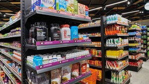 Un pasillo de supermercado con estantes repletos de diversos productos alimenticios, como cereales, proteínas en polvo y otros artículos de alimentación.