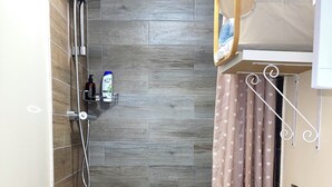 A shower with a rain showerhead, a handheld showerhead, and a shelf with toiletries. - Studio Apartment (Romford)