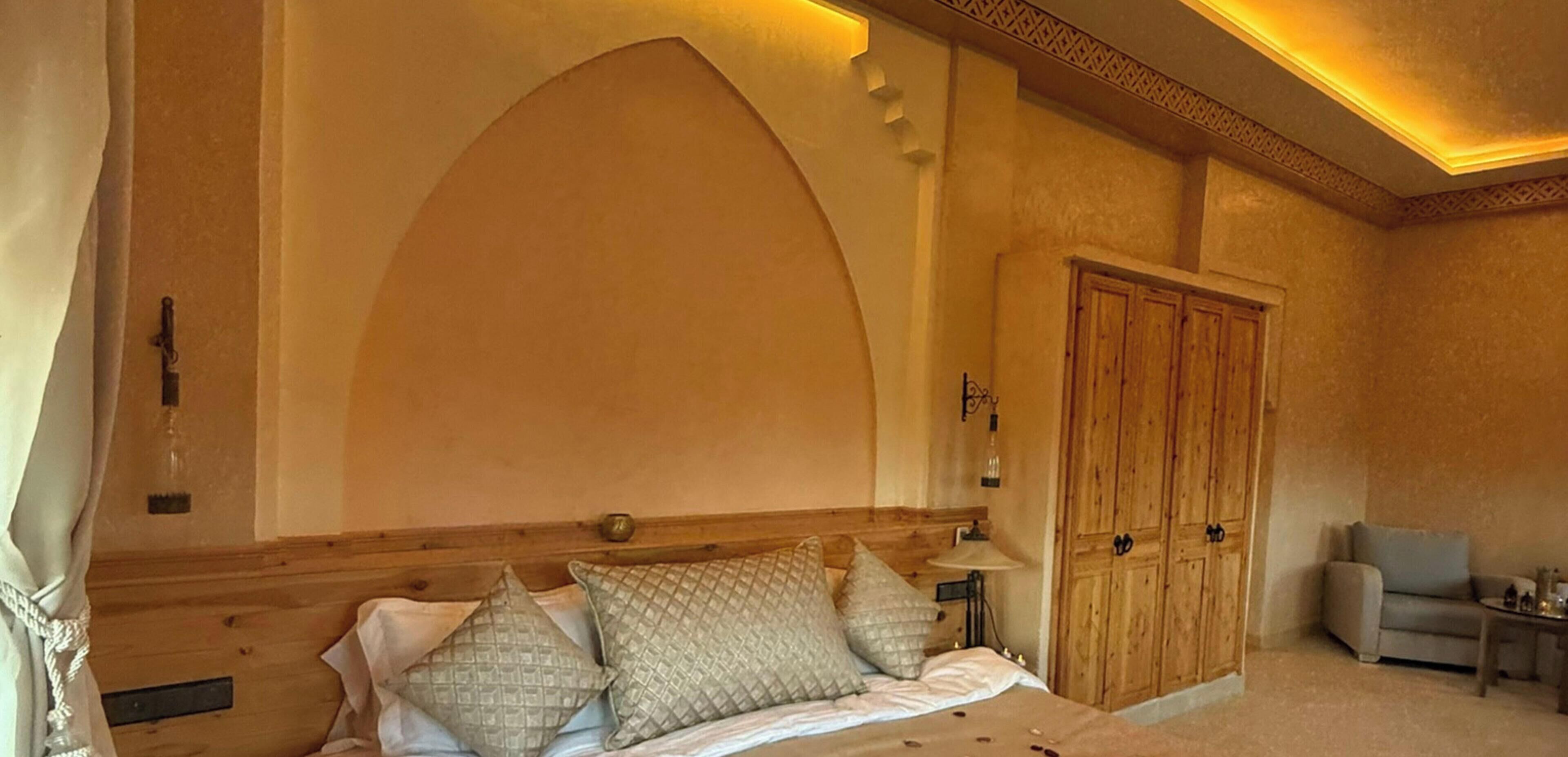 Un dormitorio con una cama grande, cabecera de madera, un armario y una mesita.