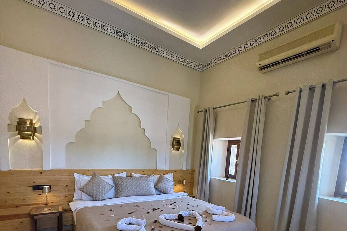 Une chambre bien rangée, avec un grand lit, des tables de chevet, un banc et un tapis à motifs.