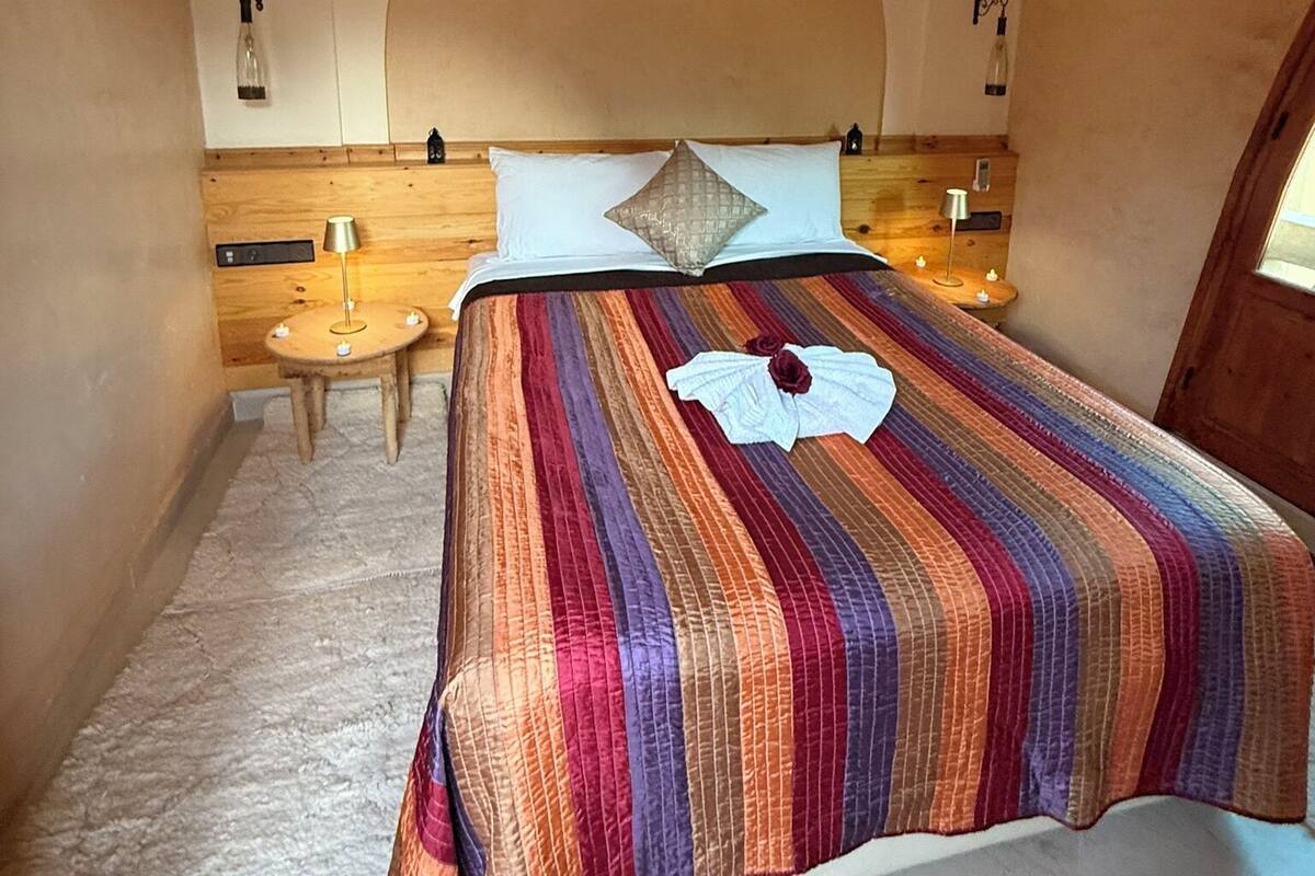 Une chambre à coucher avec un grand lit, une tête de lit en bois, une petite table ronde et une arche décorative sur le mur.