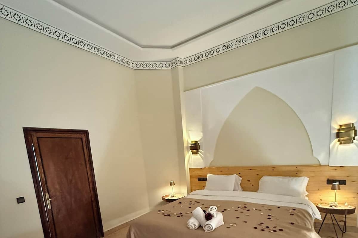 Une chambre d’hôtel avec un grand lit, deux tables de chevet, une porte en bois et un tapis à motifs.