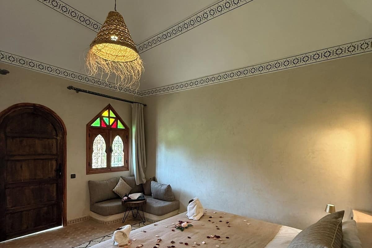 Une chambre à coucher avec un grand lit, un luminaire suspendu, une fenêtre avec des vitraux et une porte en bois.