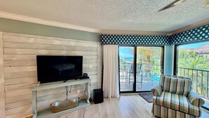A living room with a flat-screen TV on a wooden wall, a striped sofa, and a balcony with a view. - Tropical getaway awaits!!! (Saint Augustine)