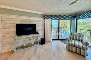 A living room with a flat-screen TV on a wooden wall, a striped sofa, and a balcony with a view. - Tropical getaway awaits!!! (Saint Augustine)
