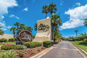 A sign for 'The Ocean Gallery' with a clear pathway leading to it, surrounded by palm trees and well-maintained landscaping.