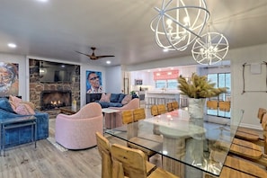 A modern living room with a fireplace, a dining area with a glass table, and a kitchen in the background. - Rest Ashored - Lake Burton 4BR retreat with hot tub, boat slip, fire pit. (Tiger)