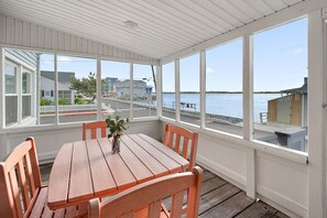 A covered patio with a wooden table and chairs, large windows with a view of a waterfront and buildings. - House with Bayview, Walk to the Beach & Boardwalk (Ocean City)