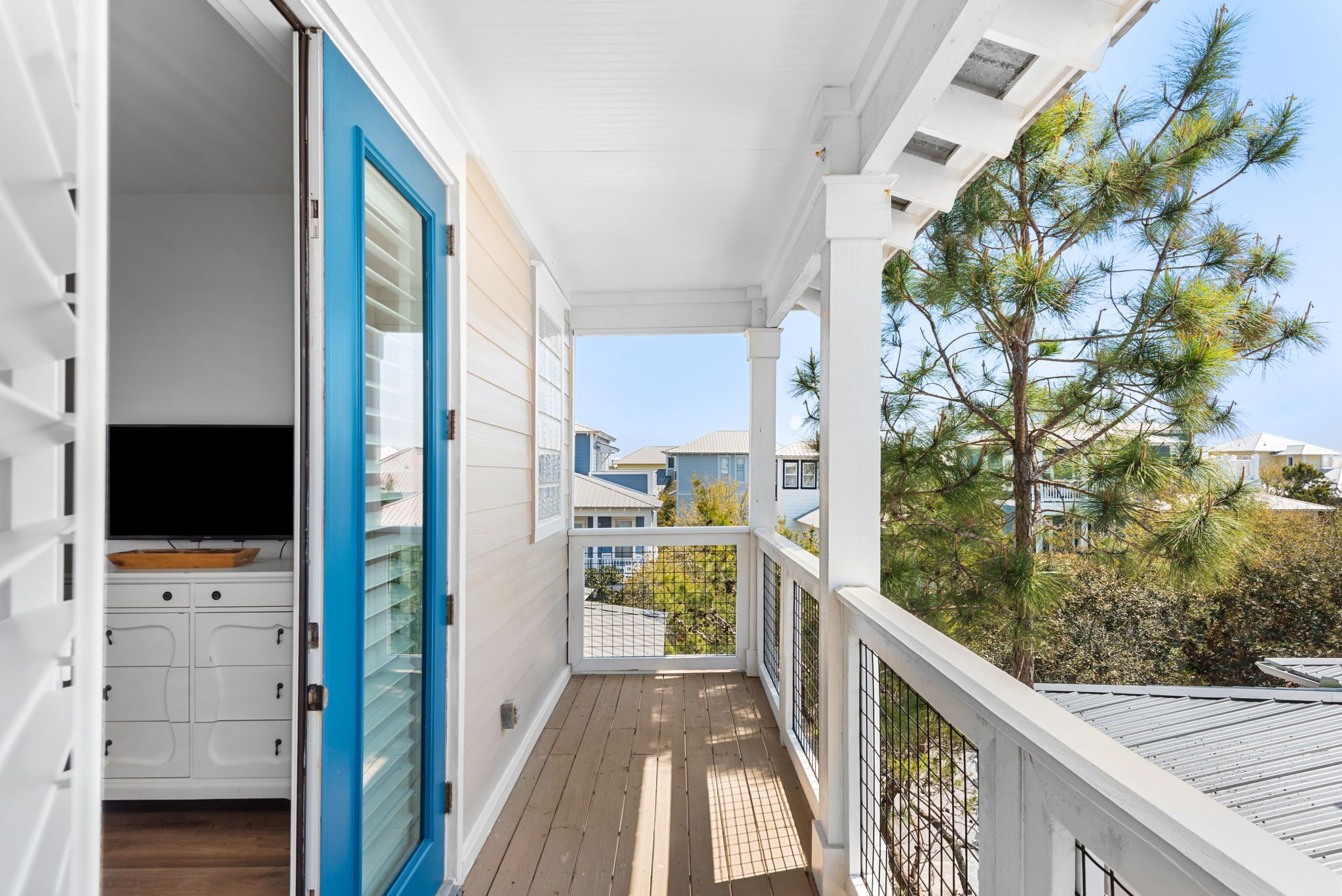 A covered porch with a view of a pine tree, a white door, and a small kitchen area with cabinets.
