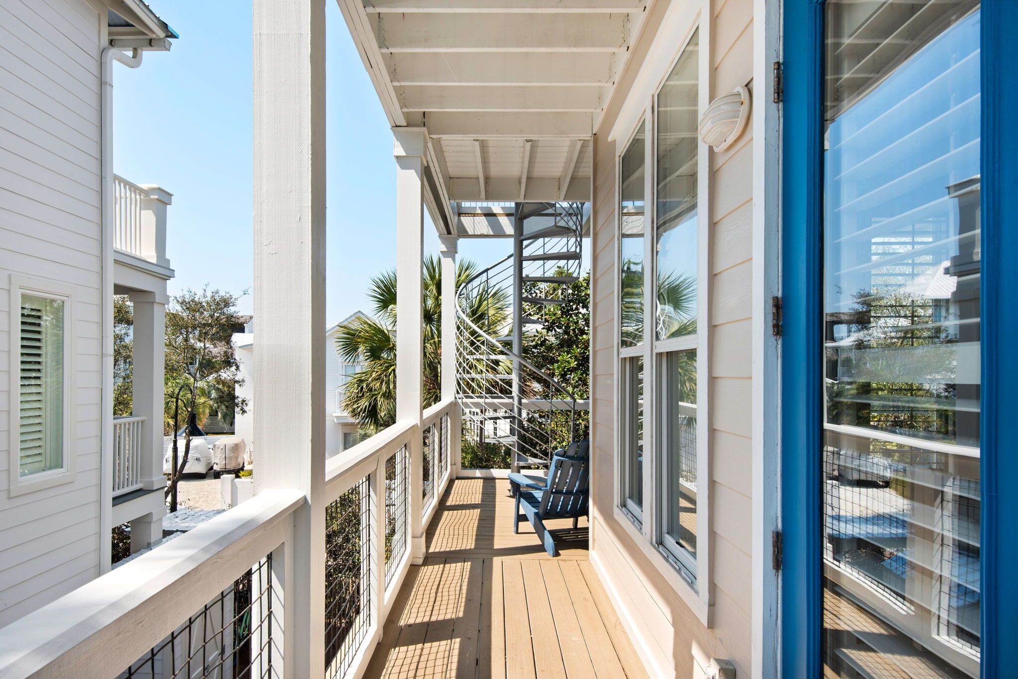 A covered porch with a spiral staircase, a white building, and a blue door.